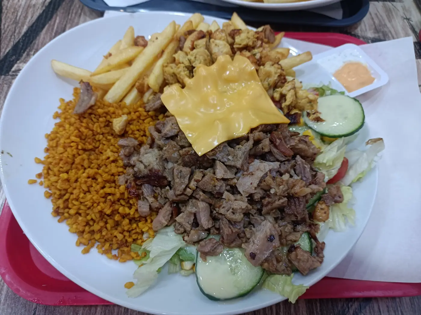 Une assiette Volcano : kebab, poulet, fromage fondu, frites, blé et salade, sur un plateau rouge