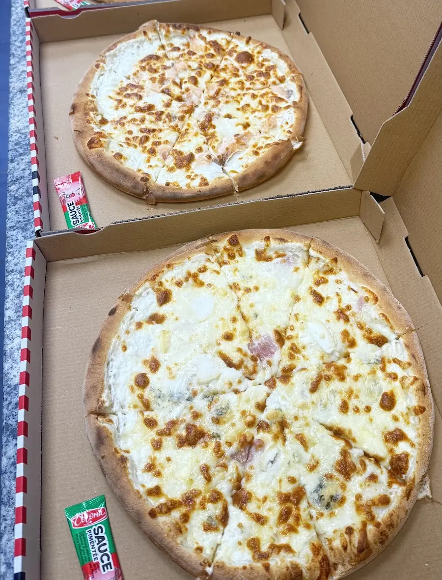 Quatre pizzas à base crème dans leurs boîtes, à emporter